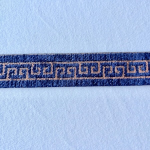 May include: A navy blue ribbon featuring a gold Greek key pattern. This decorative trim is suitable for crafts or sewing. The design is a classic, geometric motif, often used in borders.