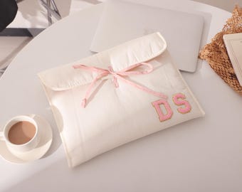 May include: A white fabric pouch with a pink ribbon tied around it. The pouch has the letters "DS" embroidered on it in pink and gold thread.