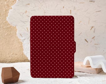Puede incluir: Una funda de color burdeos con un estampado de lunares. La funda tiene una parte superior redondeada y una pequeña pestaña en el lado derecho. El fondo es una superficie texturizada blanquecina con una forma geométrica de madera marrón y un objeto decorativo blanco.