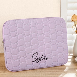 Op de afbeelding: Een lavendelkleurige, gewatteerde laptophuls met de naam "Sylvia" geborduurd op de voorkant.