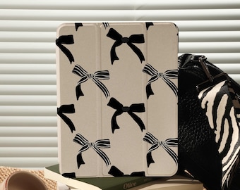 May include: A beige iPad case with a black bow pattern. The case is on top of a stack of books and a black and white zebra patterned bag.