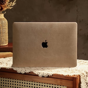 Könnte beinhalten: Ein brauner Laptop mit einem Apple-Logo auf dem Deckel. Der Laptop steht auf einer weißen Tischdecke auf einem Holztisch.