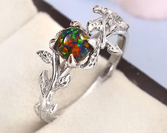 May include: A silver ring with a black opal gemstone set in a floral design. The ring features a delicate stem with leaves and a single opal in the center.