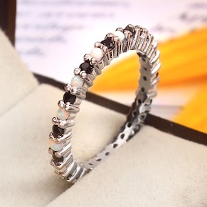 Peut inclure: Une bague en argent avec des pierres précieuses noires et blanches alternées. La bague est placée dans une boîte avec un intérieur blanc.