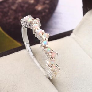 May include: A silver band ring with a zig-zag pattern of white opal stones.