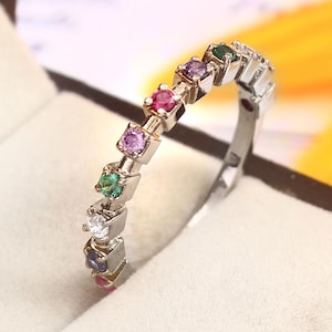 May include: A silver band ring with a row of colorful gemstones. The stones are set in a square shape and are arranged in a rainbow pattern. The ring is in a white box.