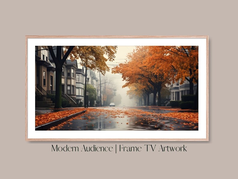 Op de afbeelding: Een mistige straat met bomen in herfstkleuren. De bladeren vallen van de bomen en bedekken het natte trottoir. De huizen in de straat zijn zichtbaar op de achtergrond.