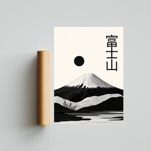 May include: A black and white minimalist art print featuring Mount Fuji with a snow-capped peak, a black sun, and Japanese text. A brown cylindrical tube is next to the print. The artwork is on a cream-colored background.