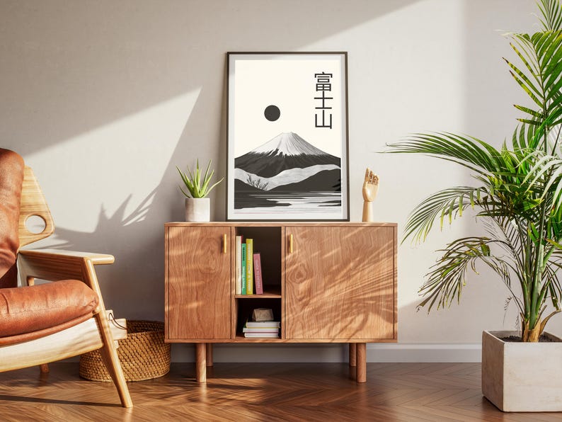 May include: A framed black and white art print featuring a mountain landscape with Japanese text. The artwork is displayed on a wooden cabinet with a plant and a wooden hand sculpture. The room has a modern, minimalist aesthetic.