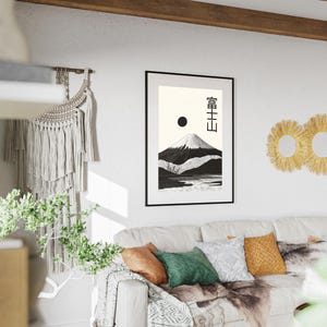 May include: A framed black and white print of a mountain landscape with Japanese text. The artwork depicts a snow-capped mountain, a lake, and a black sun against a cream background. The print is displayed above a white sofa with colorful pillows.