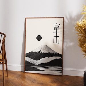 May include: Framed art print featuring a black and white illustration of Mount Fuji with a black sun and Japanese characters. The artwork has a minimalist style and is displayed in a wooden frame.