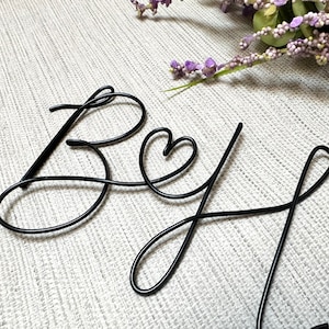 Könnte beinhalten: Schwarze Metalldrahtskulptur des Wortes "Bey" mit einem Herzen in der Mitte des "y".