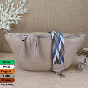 Op de afbeelding: Een beige leren heuptas met een ritssluiting en een kleurrijke geweven band. De band heeft blauwe, witte en grijze strepen.