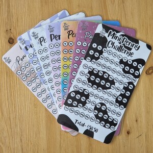 May include: A set of colourful penny challenge cards with a black and white cow print card that says "Mini Penny Challenge" and "Total - £50.50". Each card has a grid of circles with numbers representing the value of each penny.