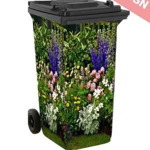 May include: A black wheelie bin with a colourful floral design. The design features a variety of flowers, including pink peonies, purple delphiniums, and white daisies. The bin is on a white background.
