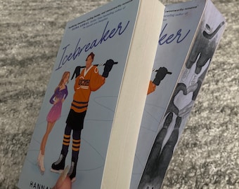Puede incluir: Dos libros de bolsillo con el título "Icebreaker" en la portada. El libro de la izquierda tiene una portada azul con una niña y un niño patinando sobre hielo. El libro de la derecha tiene una portada azul con un par de patines de hielo.
