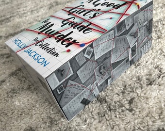 May include: A book titled "A Good Girl's Guide to Murder" by Holly Jackson. The cover features a red string connecting various pieces of paper with handwritten notes and a grid pattern.