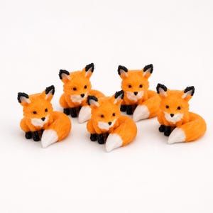 Könnte beinhalten: Ein Set aus fünf Miniatur-Fuchsfiguren, jeweils mit leuchtend orangefarbenem Fell, weißen Akzenten an Brust und Schwanzspitze sowie schwarzen Ohren und Pfoten. Die Füchse sind in sitzender Position dargestellt, mit ihren buschigen Schwänzen.