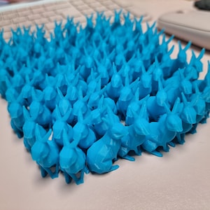 Könnte beinhalten: Eine große Gruppe von leuchtend blauen, im 3D-Druck hergestellten Hasenfiguren, die in Reihen angeordnet sind.