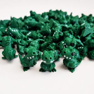 Könnte beinhalten: Eine große Ansammlung kleiner, dunkelgrüner Dinosaurierfiguren aus Kunststoff. Jede Miniaturfigur stellt einen zweibeinigen Dinosaurier mit strukturierter Oberfläche, schwarz bemalten Augen und weiß bemalten Zähnen dar.