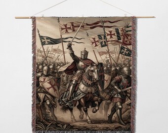 May include: Woven tapestry depicting a medieval battle scene with knights on horseback and foot soldiers. The artwork features a knight in shining armor on a horse, holding a sword aloft, surrounded by soldiers and flags with red crosses. The tapestry is fringed.