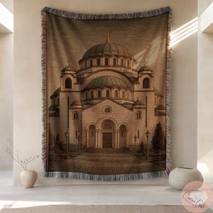 Könnte beinhalten: Ein gewebtes Wandtuch mit einer detaillierten Illustration einer Kathedrale mit mehreren Kuppeln und architektonischen Details. Das Wandtuch hat eine beige-braune Farbpalette mit einem Fransenrand, geeignet für die Heimdekoration.