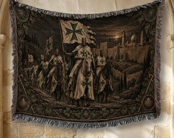 May include: A woven tapestry blanket featuring a dark, detailed scene of armored knights on horseback carrying flags with green crosses. The knights ride toward a stone fortress under a moonlit sky, framed by a decorative border with leaf motifs.