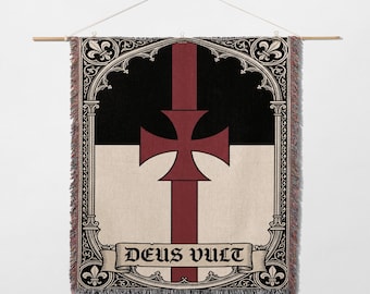 May include: Woven wall hanging featuring a Templar cross design. The banner has a black and cream background with a red cross and vertical stripe. The words "DEUS VULT" are displayed on a banner at the bottom. The banner is hung from a wooden rod.