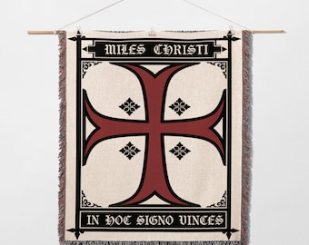 May include: Woven wall hanging featuring a large red cross with black trim and floral accents on a cream background. The text "MILES CHRISTI" and "IN HOC SIGNO VINCIS" are displayed in black. The tapestry is hung from a wooden rod.