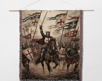 May include: Woven tapestry featuring a medieval battle scene. A knight on horseback raises a sword, leading a charge of soldiers. The tapestry displays flags with red crosses, helmets, shields, and a decorative fringe.