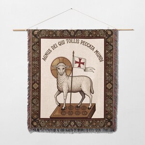 Könnte beinhalten: Ein gewebter Wandbehang mit einem Lamm, das eine Flagge mit einem Kreuz hält. Das Lamm steht auf einem Buch mit kreisförmigen Designs. Der Text "AGNUS DEI QUI TOLLIS PECCATA MUNDI" ist kreisförmig angeordnet. Der Rand hat ein detailliertes geometrisches Muster.