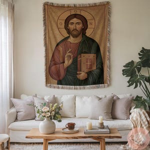 Könnte beinhalten: Ein gewebtes Wandbehang, das eine religiöse Figur mit Heiligenschein zeigt, die ein Buch hält. Die Figur trägt rote und grüne Gewänder. Der Wandbehang wird an einer Wand über einem weißen Sofa mit Kissen, einem Holztisch und einer Blumenvase ausgestellt.
