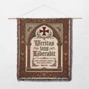 Könnte beinhalten: Ein Wandbehang aus Tapisserie mit cremefarbenem Hintergrund und einer dekorativen Bordüre in Braun- und Burgundertönen. Das Design umfasst ein Kreuz, verzierten Text und den Satz "DIE WAHRHEIT WIRD EUCH FREI MACHEN" aus Johannes 8:32.