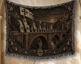 May include: A woven tapestry blanket featuring a dark, detailed scene of knights on horseback crossing a stone bridge toward a castle. The border is decorated with a pattern of pears and leaves, with a central cross emblem at the bottom edge.