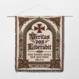 Könnte beinhalten: Ein Wandbehang aus Tapisserie mit cremefarbenem Hintergrund und aufwendigen burgunderroten und grünen Details. Das Design umfasst ein Kreuz, dekorative Schnörkel und den lateinischen Satz "Veritas Vos Liberabit" mit der englischen Übersetzung "The Truth Shall Set You Free" und dem Bibelvers Johannes 8:32.