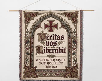 May include: A tapestry wall hanging with a cream background and ornate burgundy and green detailing. The design includes a cross, decorative scrollwork, and the Latin phrase "Veritas Vos Liberabit" with the English translation "The Truth Shall Set You Free" and the Bible verse John 8:32.