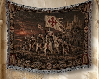 May include: A woven tapestry throw blanket featuring a scene of knights on horseback carrying white flags with red crosses, approaching a stone castle at sunset. The border displays castle motifs and red cross emblems with fringed edges.