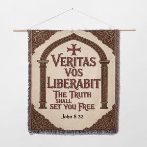 Puede incluir: Un tapiz de pared tejido con el texto "Veritas Vos Liberabit The Truth Shall Set You Free" en letras burdeos. El diseño incluye una cruz y bordes decorativos en burdeos y crema. La pancarta está suspendida de una barra de madera.