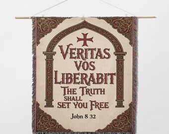 May include: A woven wall hanging with the text "Veritas Vos Liberabit The Truth Shall Set You Free" in burgundy lettering. The design includes a cross and decorative borders in burgundy and cream colors. The banner is suspended from a wooden rod.
