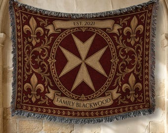 May include: A woven throw blanket featuring a deep red background with a central beige Maltese cross inside a circular border. The design includes four fleur-de-lis motifs, a banner at the top reading EST. 2021, and a banner at the bottom reading FAMILY BLACKWOOD.