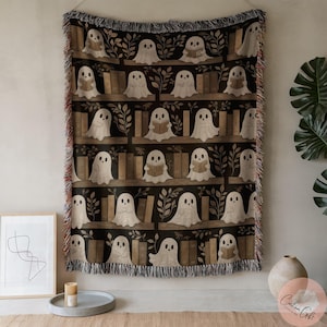 May include: A woven throw blanket with a repeating pattern of friendly ghost characters reading books on shelves. The background is black with brown bookshelves and green leaf accents. The blanket has a fringed edge.