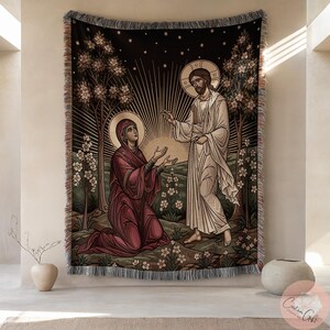Könnte beinhalten: Gewebte Tapisserie mit einer religiösen Szene mit zwei Figuren in einem Garten. Das Kunstwerk zeigt eine Frau, die vor einem Mann kniet, mit einer strahlenden Sonne und Sternen im Hintergrund. Die Tapisserie hat einen schwarzen Rand mit Fransen.