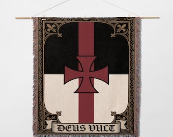 May include: Woven wall hanging featuring a Templar cross design. The flag has a black top, a white bottom, and a central burgundy stripe and cross. The phrase "DEUS VULT" is displayed on a banner at the bottom. The edges are fringed.
