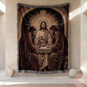 May include: Woven tapestry depicting a religious scene with three figures gathered around a table. The central figure, with a halo, is breaking bread. The tapestry features a dark background with a decorative border and fringe.