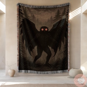 May include: A woven tapestry depicting a dark illustration of a cryptid creature with large wings and glowing red eyes, set against a forest backdrop. The tapestry has a fringed edge and is displayed on a wall.