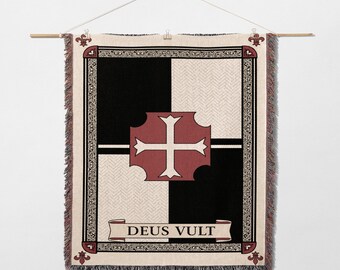 May include: A tapestry with a black and cream checkered pattern, featuring a red cross design at the center. The tapestry has a decorative border and the words "DEUS VULT" on a banner. It is hung from a wooden rod.