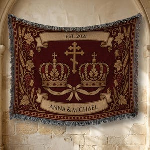 Könnte beinhalten: Eine gewebte Wohndecke in Dunkelrot mit einem zentralen Motiv aus zwei verzierten Kronen und einem orthodoxen Kreuz. Die Decke zeigt beige Banner mit dem Text EST. 2021 und ANNA & MICHAEL, umrahmt von dekorativen Weinreben- und Weizenmotiven.