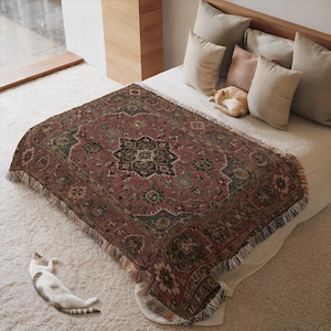 Könnte beinhalten: Eine gewebte Decke mit einem traditionellen persischen Teppichdesign in Burgunder-, Grün- und Beigetönen. Die Decke hat einen Fransenrand und ist über ein Bett drapiert. Eine Katze schläft auf dem Bett und eine andere liegt auf dem Boden.