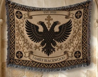 May include: A woven throw blanket featuring a black double-headed eagle centered above the text FAMILY BLACKWOOD and below the text EST. 2021. The design includes a central cross, ornate floral scrollwork, and a geometric border with fringe.