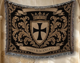 May include: A woven throw blanket featuring a black and tan color scheme with a central shield displaying a black cross. Above the shield is a crown, and below is a banner with the text FAMILY BLACKWOOD. A top banner reads EST. 2021.